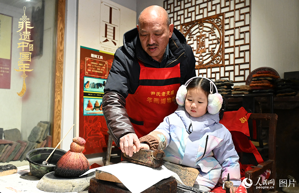 2025年1月27日，河南開封朱仙鎮(zhèn)木版年畫藝人尹國法指導小朋友研習年畫印制技藝。朱仙鎮(zhèn)木版年畫源自漢唐壁畫藝術，是中國木版年畫的鼻祖。2006年5月20日，朱仙鎮(zhèn)木版年畫經國務院批準列入第一批國家級非物質文化遺產名錄。人民網記者 王玉興攝